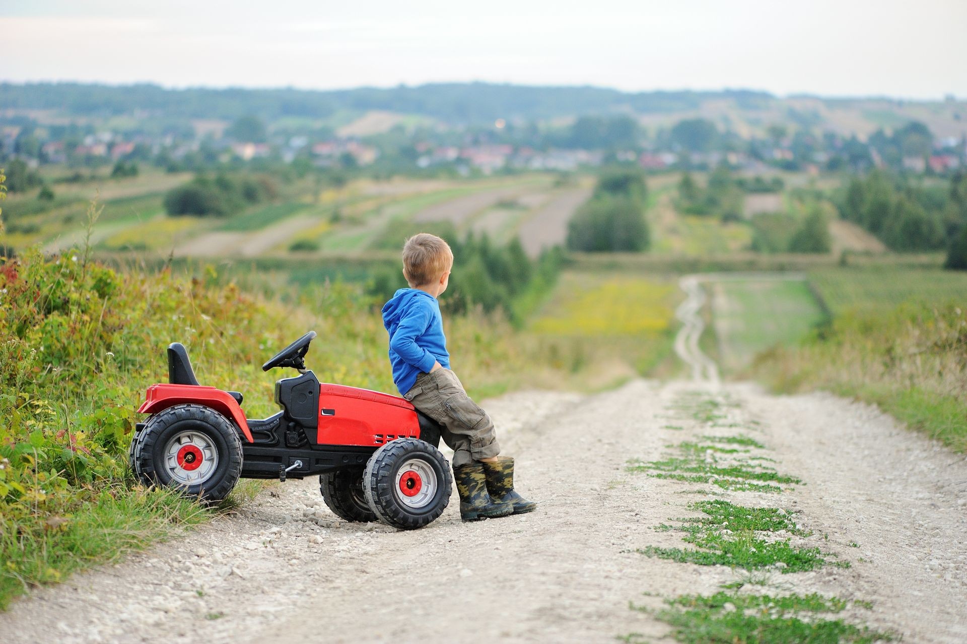 Small boy  with toy tractor. He  resting on a dirt road overlooking the valley.